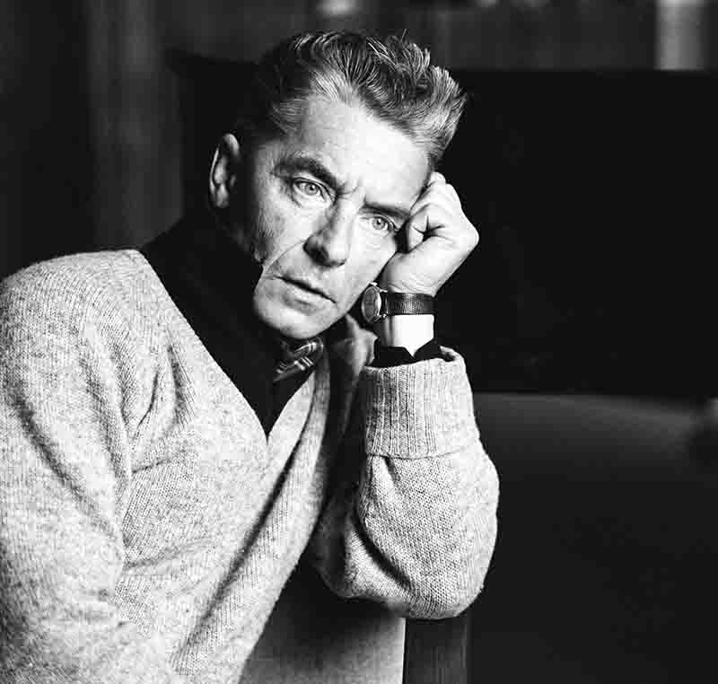 Schwarz Weiss Foto von Herbert von Karajan der einen Pullover trägt und entspannt auf einem Stuhl sitzt.