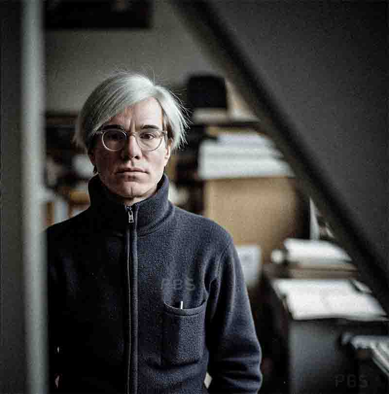 Eine Farbaufnahme von Bock-Schroeder zeigt den Künstler Andy Warhol (mit seiner markanten, hellgrauen Perücke und runden Brillengläsern) in einer mittigen Halbtotale. Er blickt direkt in die Kamera mit einem ernsten, kontemplativen Ausdruck.